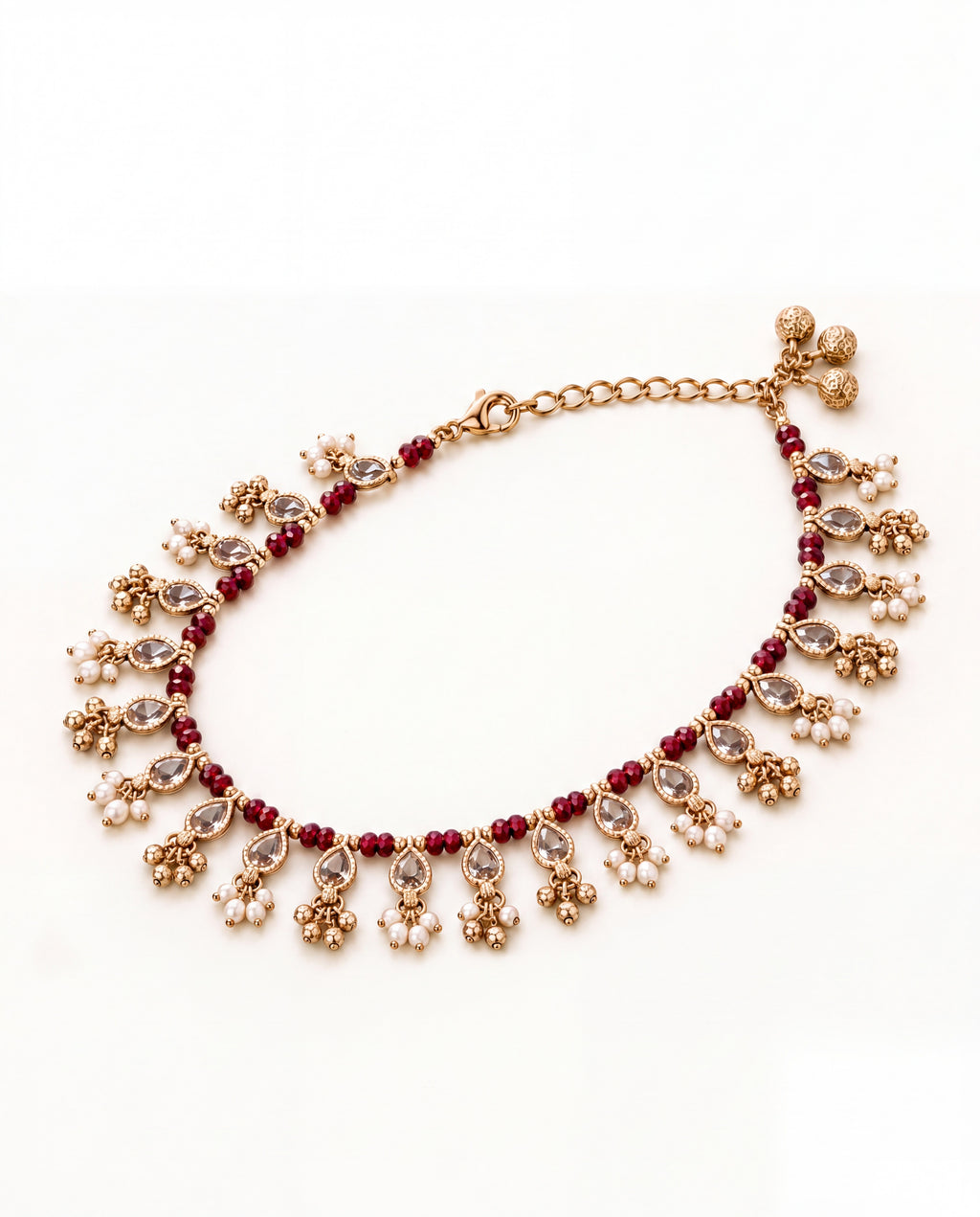 Bloom Drop red anklet laid in an oval with clear teardrop stones, red beads and pearl and bell tassels