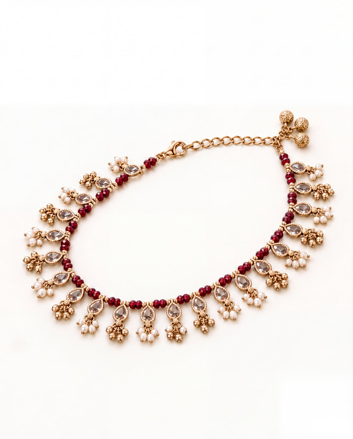 Bloom Drop red anklet laid in an oval with clear teardrop stones, red beads and pearl and bell tassels