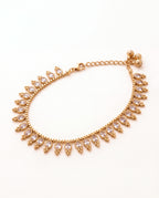 Margot Chime gold-tone anklet laid in an oval with a fringe of clear oval stones and three small bells
