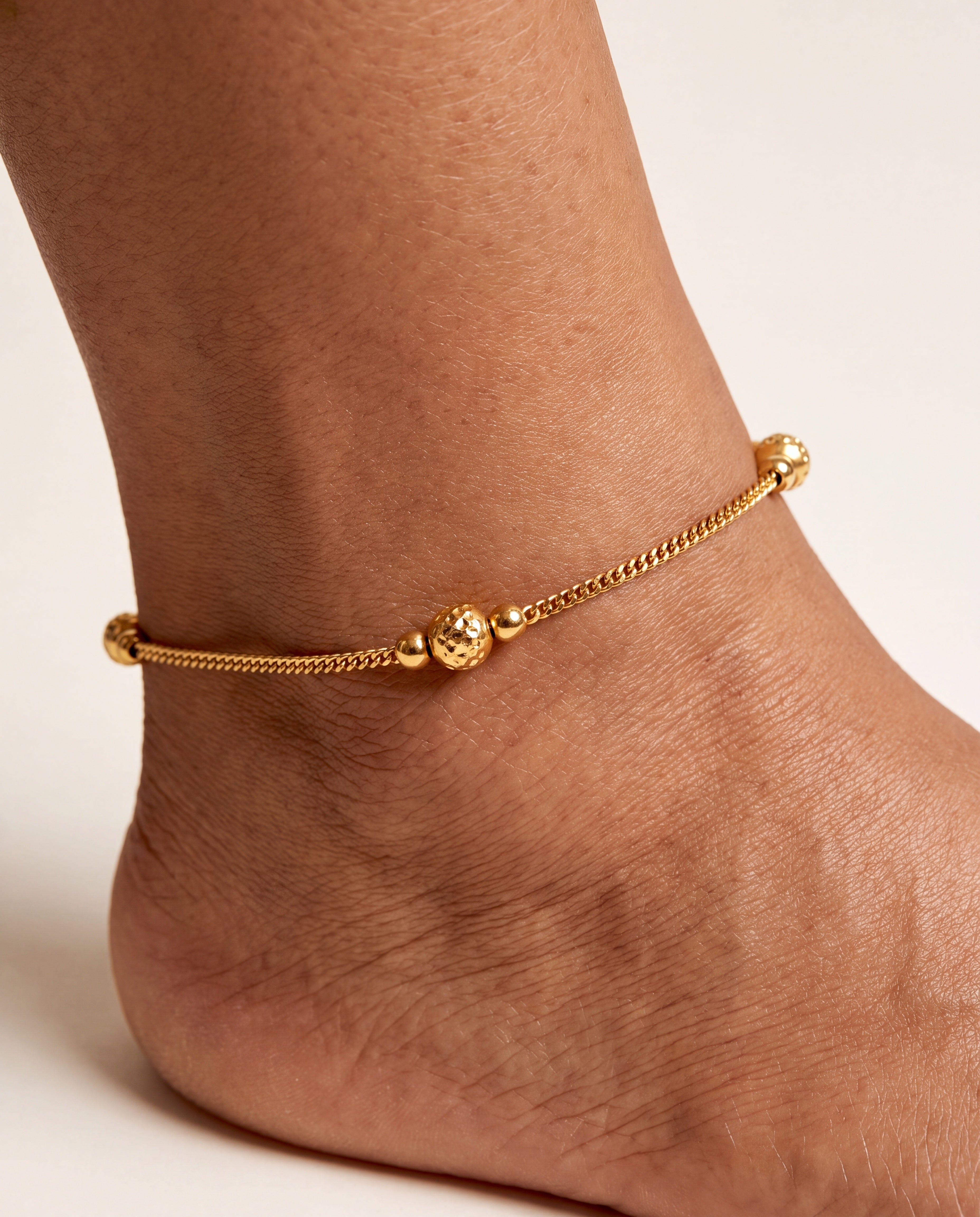 Luma Glow gold-tone anklet worn on an ankle with a textured bead station
