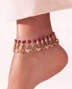 Bloom Drop red anklet worn on a raised ankle, showing teardrop stones and pearl and bell tassels