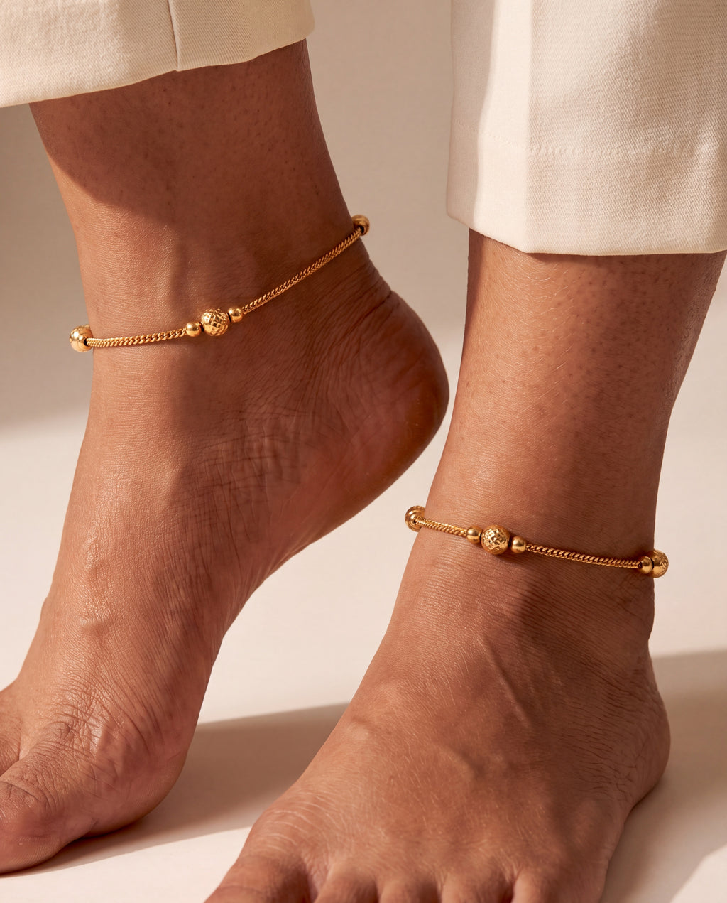 Pair of Luma Glow gold-tone anklets worn on both ankles with textured bead stations