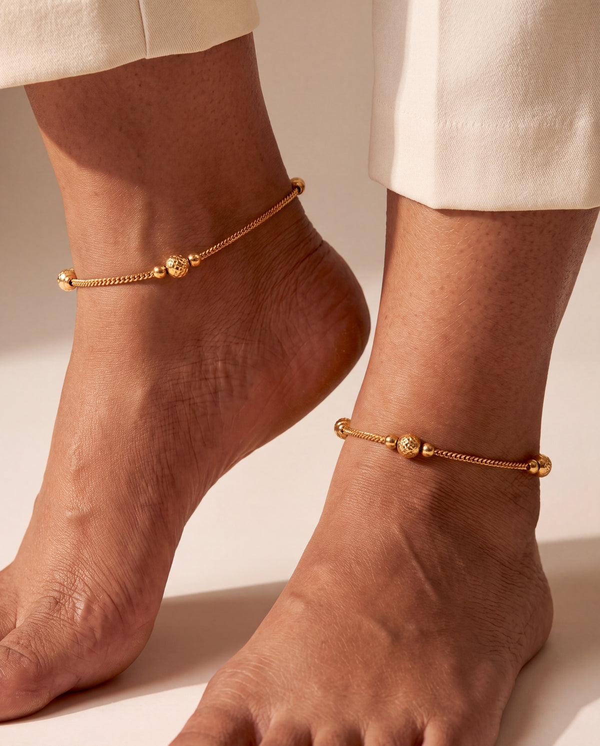 Pair of Luma Glow gold-tone anklets worn on both ankles with textured bead stations