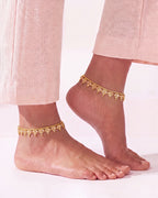 Vera gold-tone anklets worn on both ankles with blush trousers
