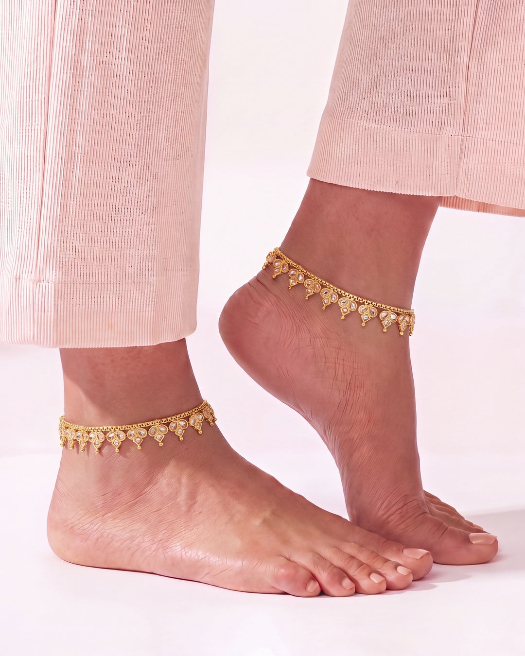 Vera gold-tone anklets worn on both ankles with blush trousers