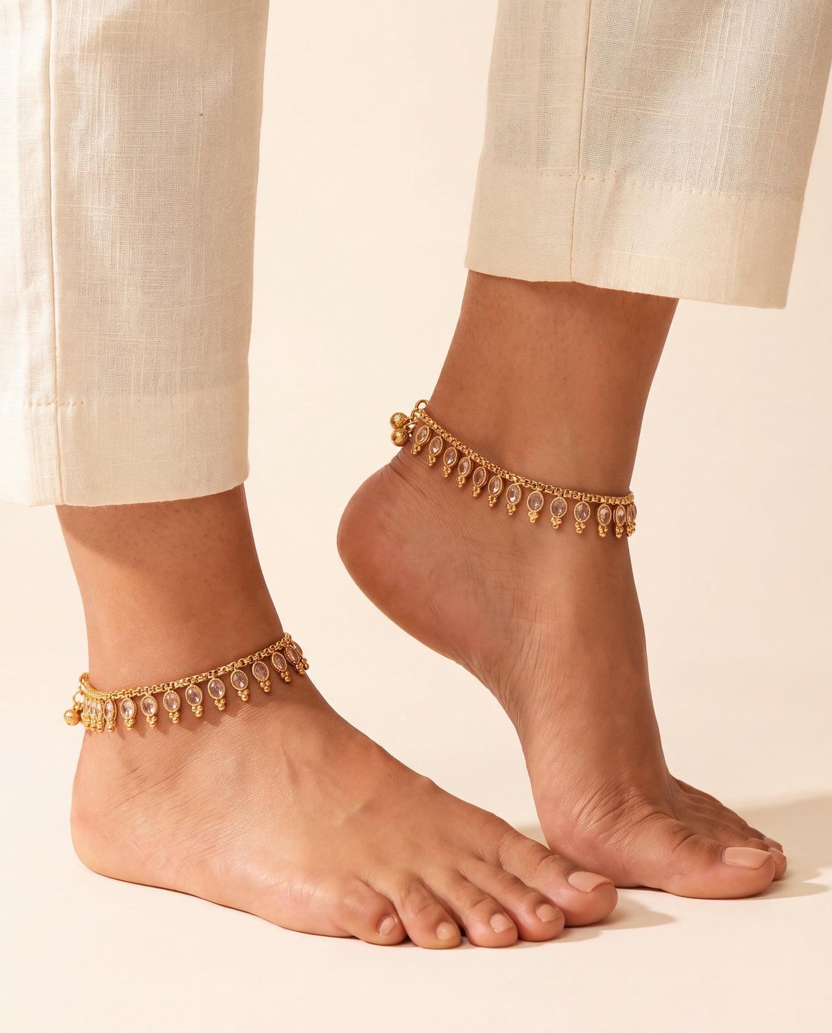 Margot Chime gold-tone anklets worn on both ankles with cream trousers