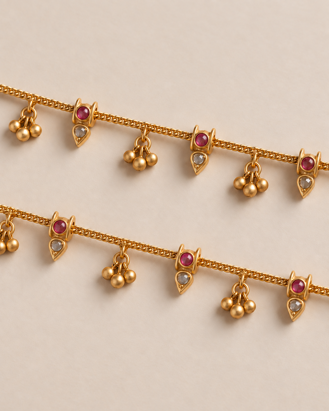 Close pair detail of matching Mira Dewdrop Anklets, gold-tone chain with three-bell clusters, clear pear stones, and pink accents