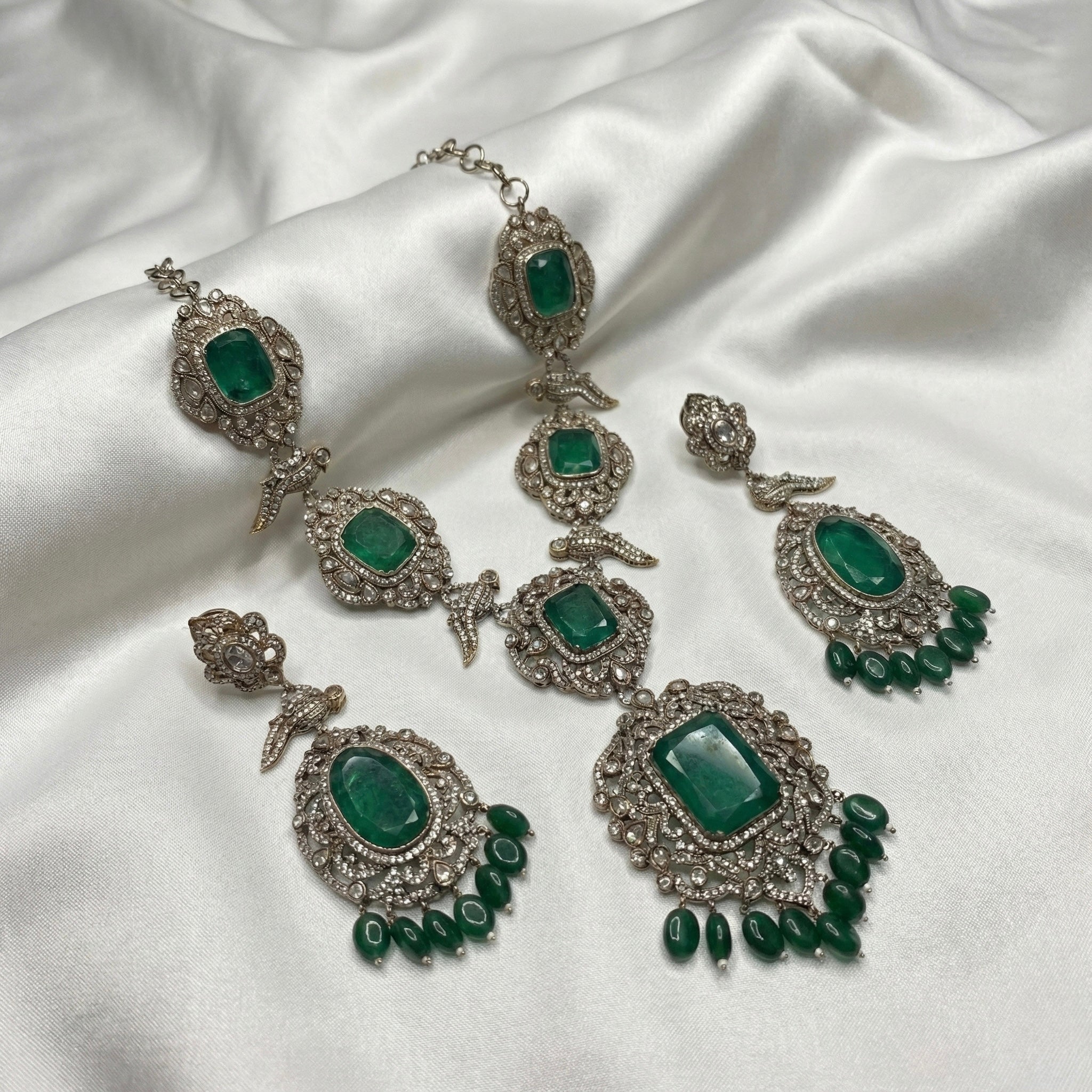 Detail flatlay of the gold-tone emerald statement necklace and matching earrings with green detailing