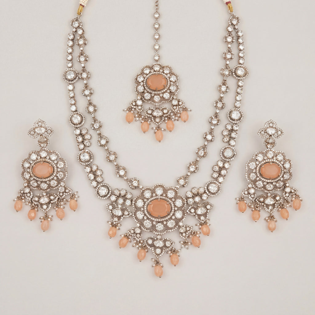 Aria Peach Necklace Set silver bib necklace with peach stones, drop earrings, and maang tikka on gray background