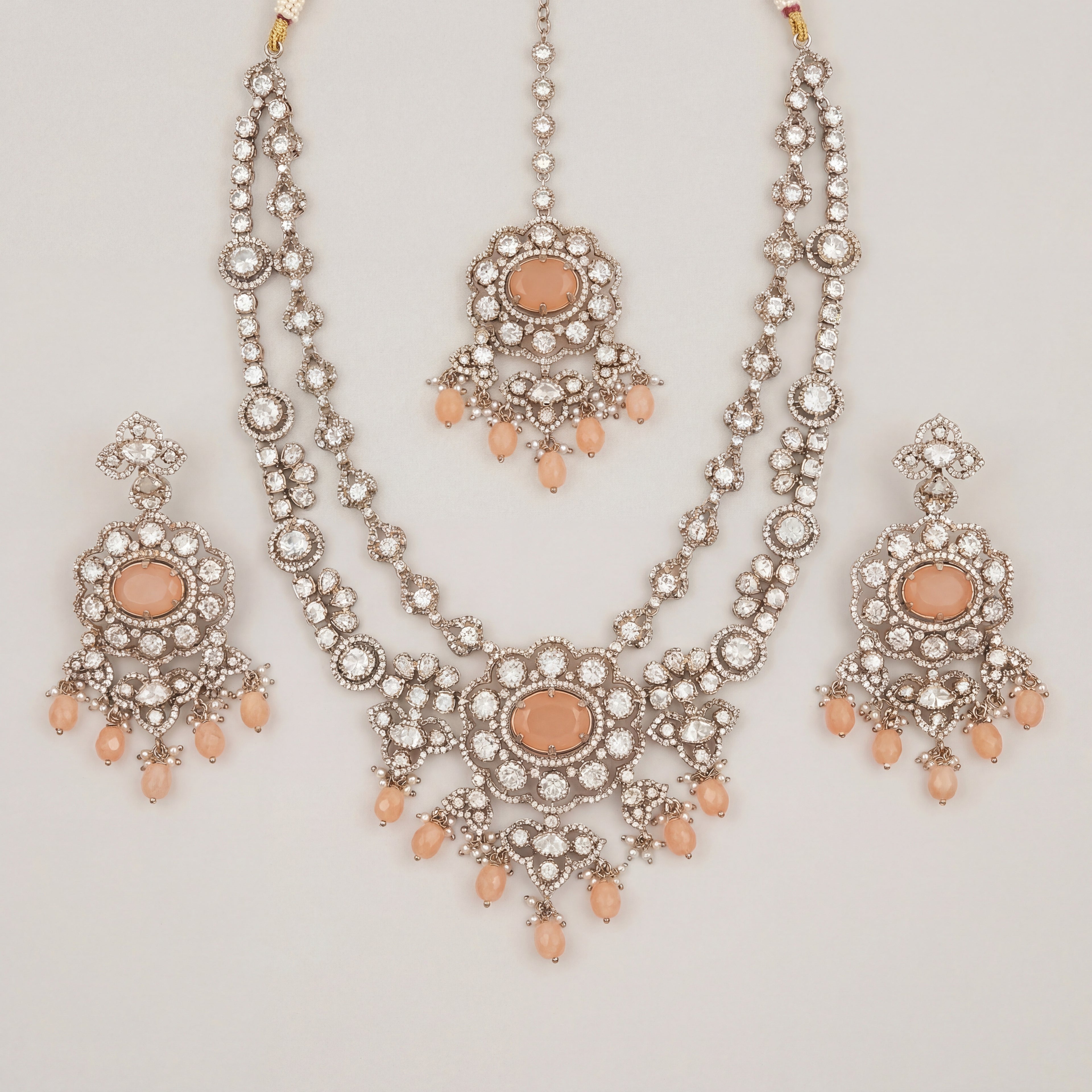 Aria Peach Necklace Set silver bib necklace with peach stones, drop earrings, and maang tikka on gray background