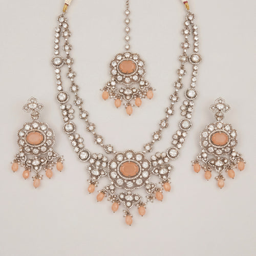 Aria Peach Necklace Set silver bib necklace with peach stones, drop earrings, and maang tikka on gray background