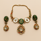 Detail flatlay of the gold-tone mother-of-pearl necklace and matching earrings with emerald accents