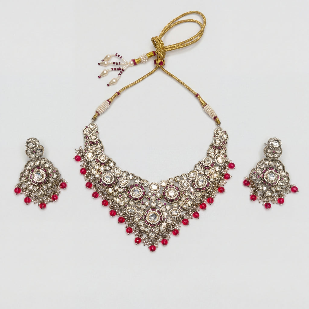 Aira Ruby Necklace Set silver kundan bib collar with ruby-red bead fringe and matching drop earrings on gray background