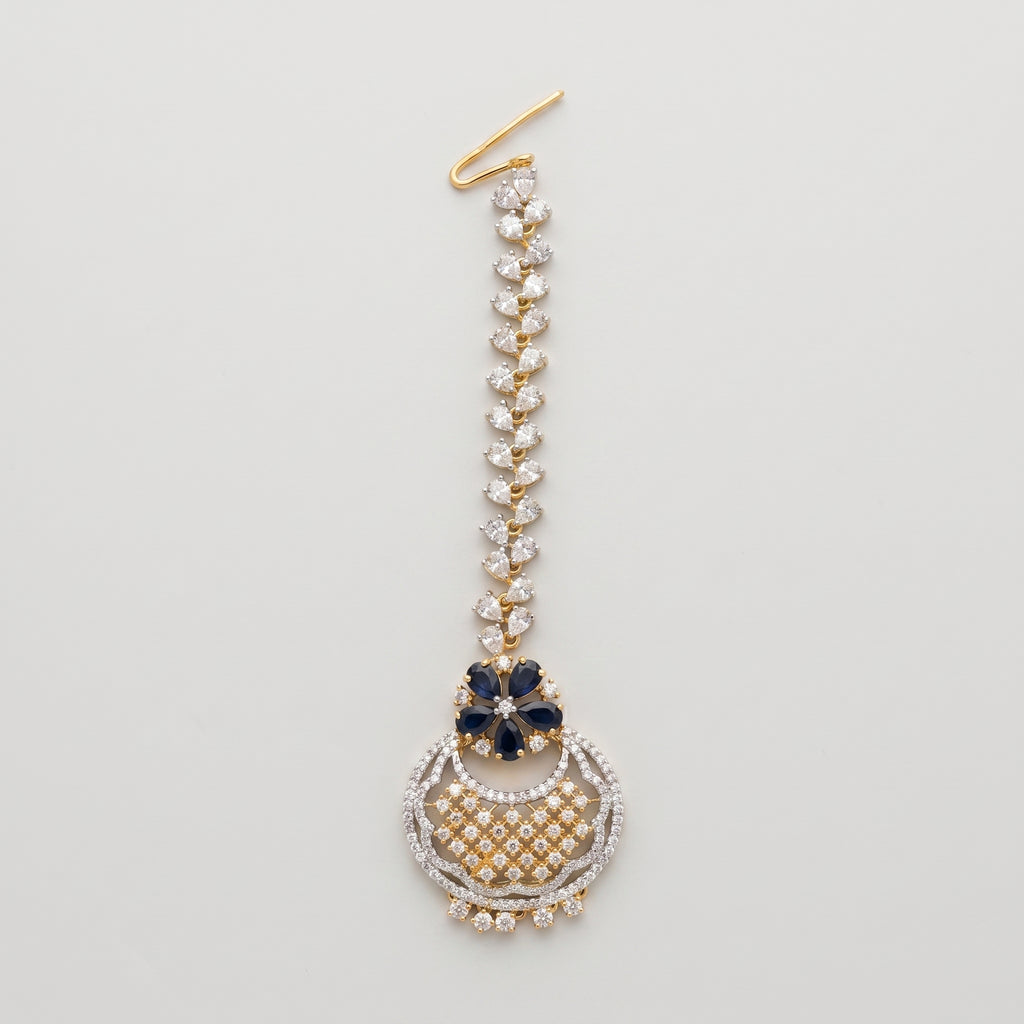 Rani Sapphire Tikka dual-tone maang tikka with blue floral accent and crescent crystal pendant on gray background