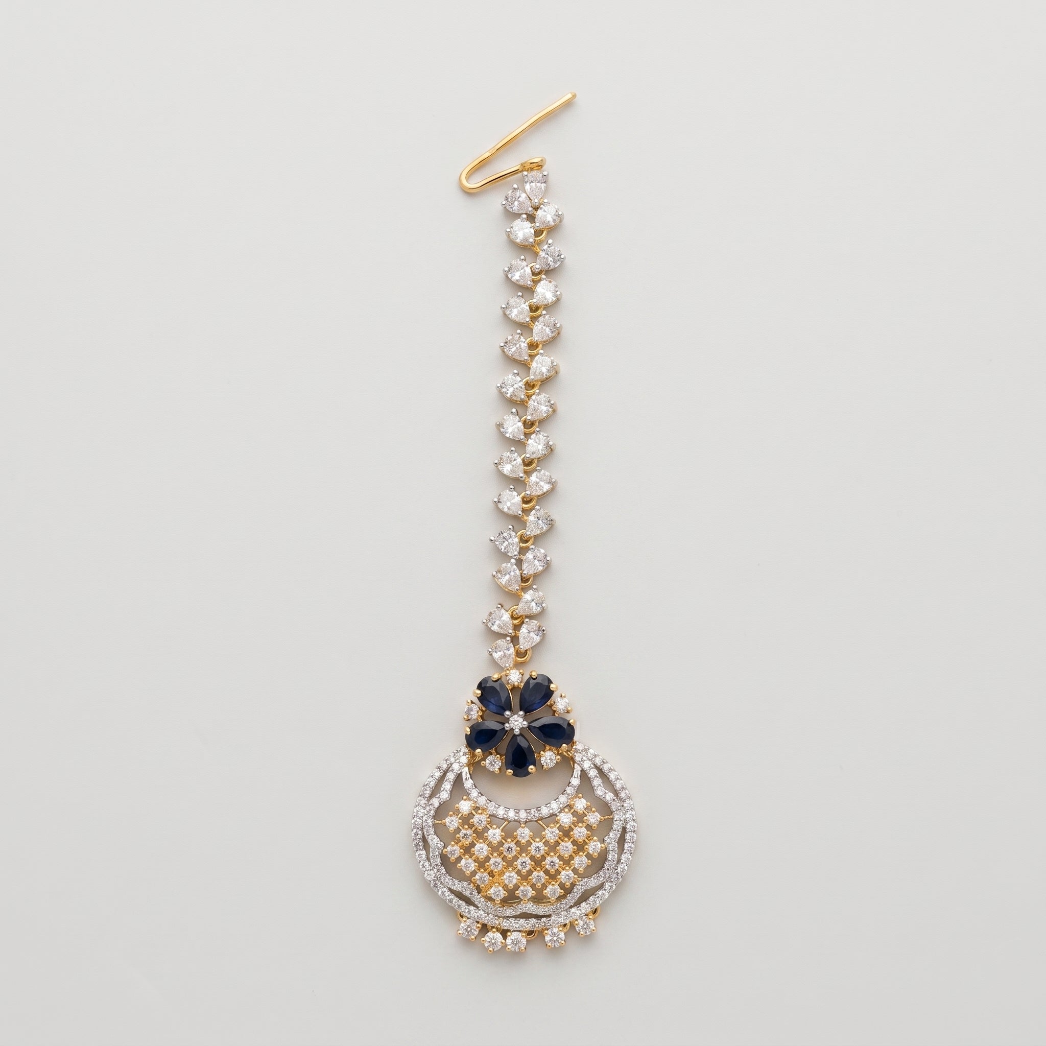 Rani Sapphire Tikka dual-tone maang tikka with blue floral accent and crescent crystal pendant on gray background