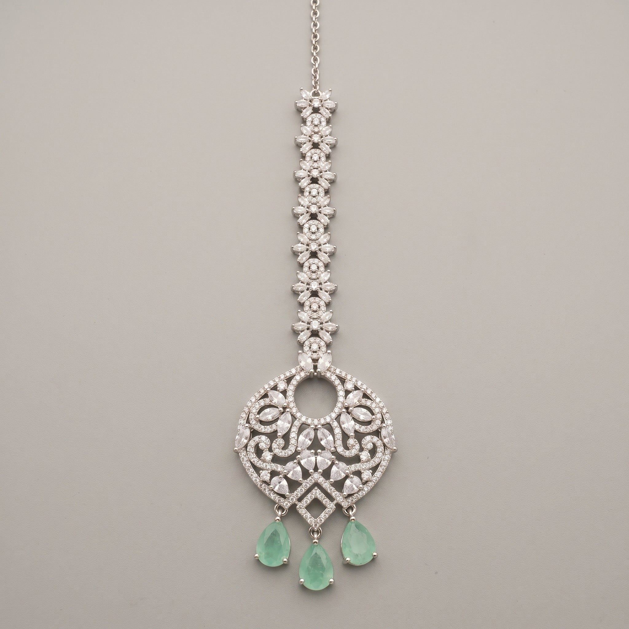 Panna Crystal Tikka silver-tone maang tikka with green teardrop drops on gray background