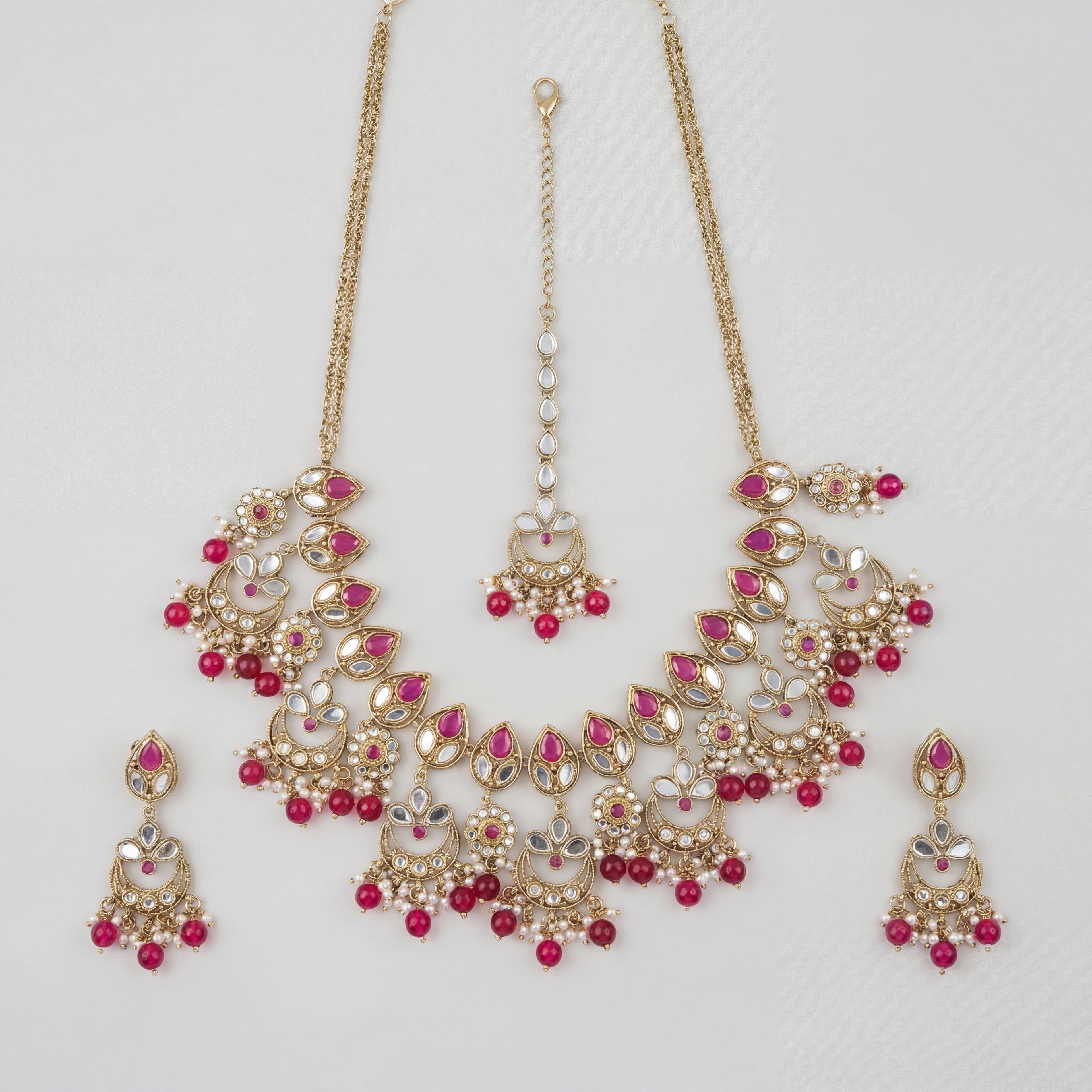 Rani Necklace Set gold kundan bib with pink stones, chandbali earrings, and maang tikka on gray background