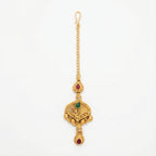 Ishara Leaf Crest Tikka antique gold maang tikka with green and red teardrop stones on gray background