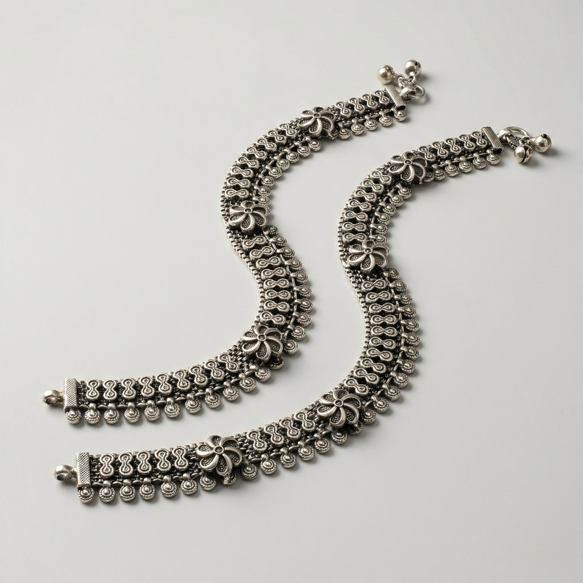 Oxidized Floral Payal pair of antique silver mesh payals with floral motifs and coin charms on gray background