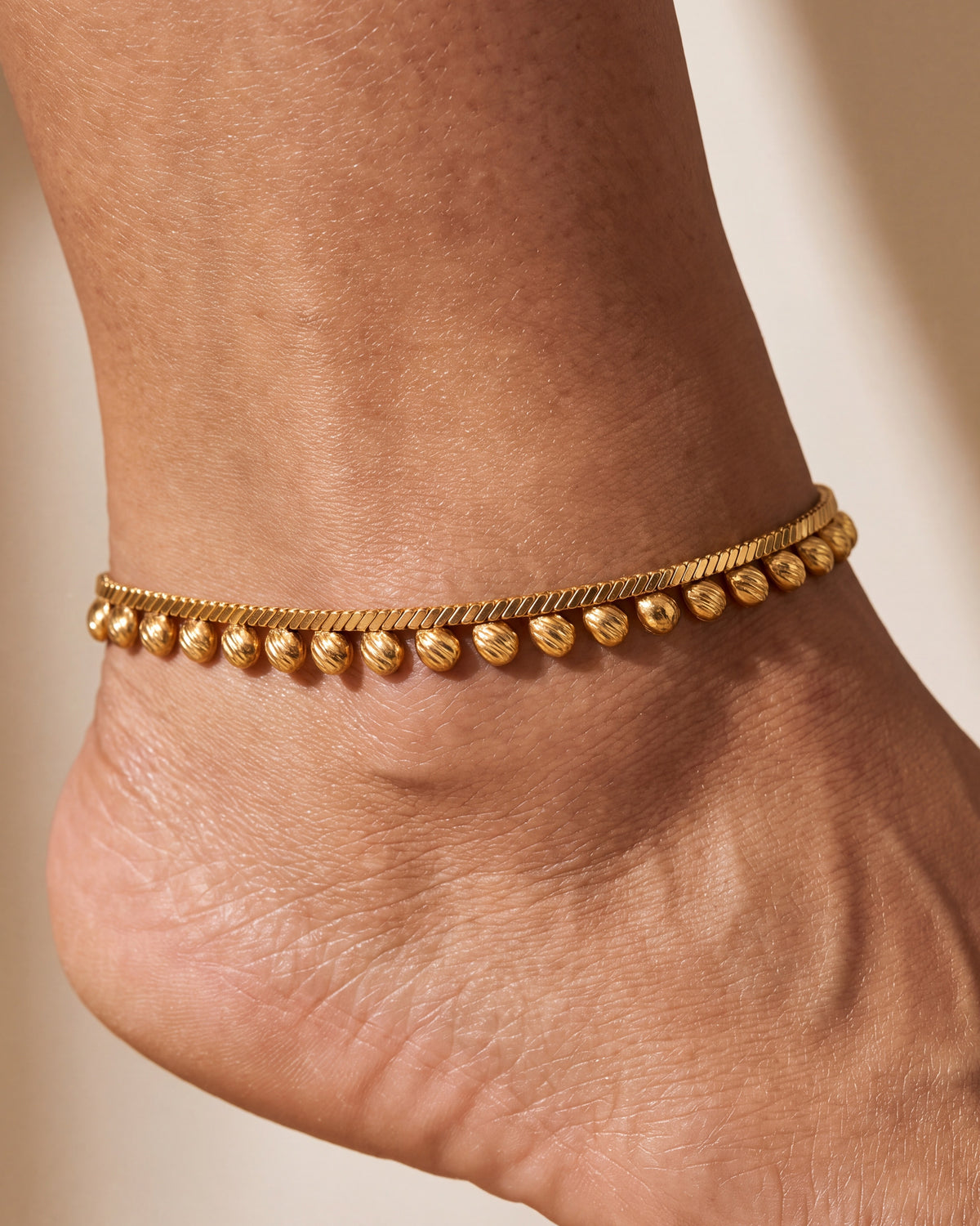 Close detail of Rani Droplet Anklet, gold-tone chain with smooth and textured droplet charms