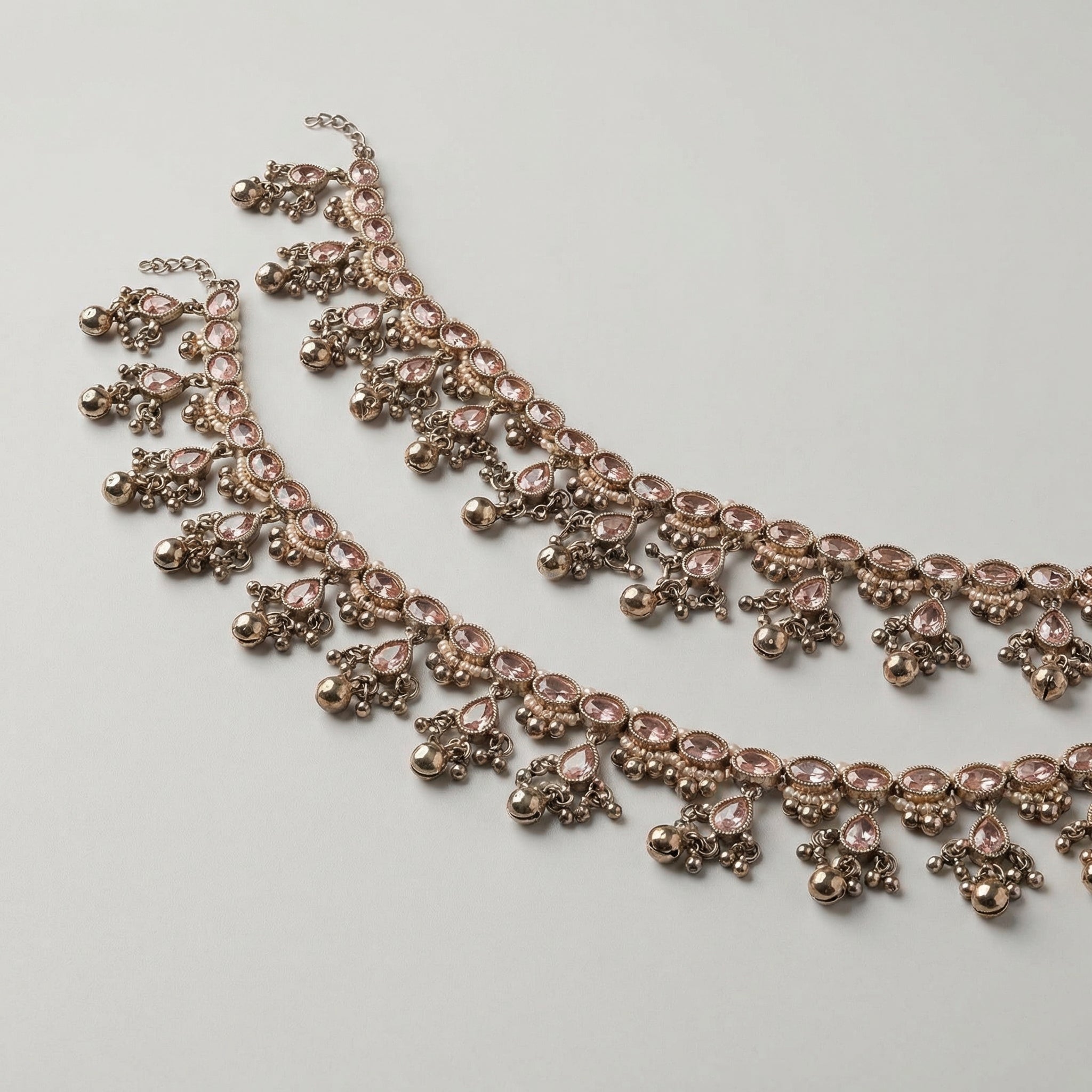 Antique Zircon Anklet pair of oxidized silver-tone payals with pink teardrop stones and ghungroo bells on gray background